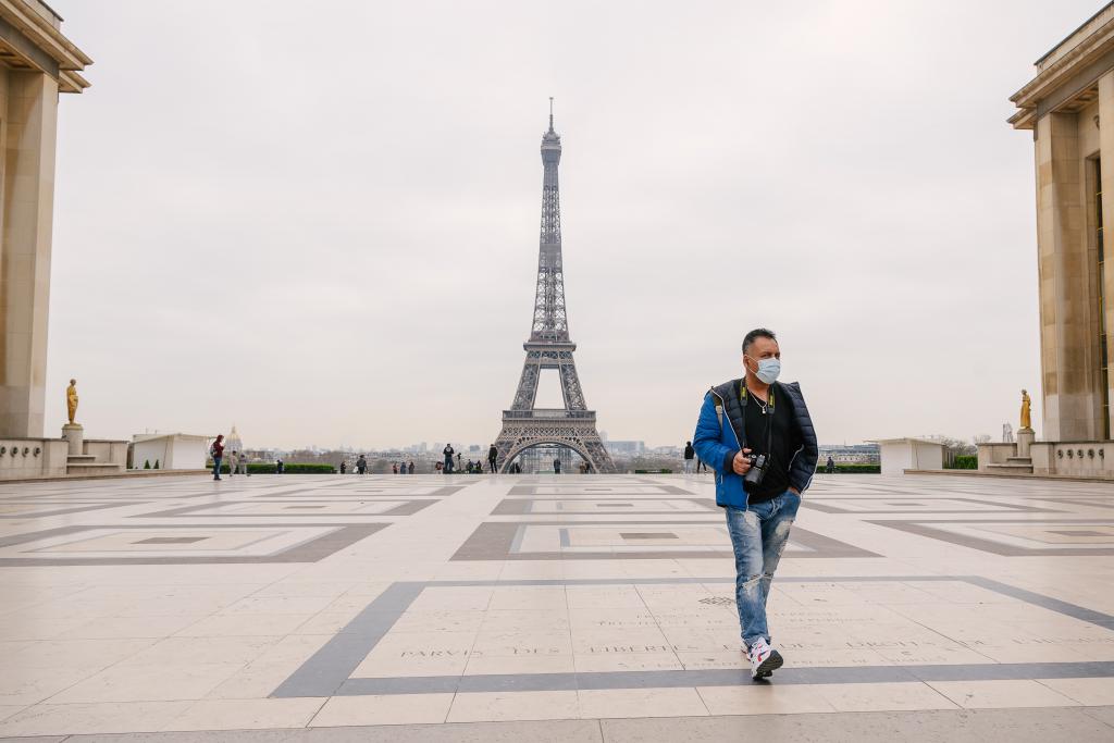 Homme avec un masque chirurgical marchant sur l'esplanade du Trocadéro avec la Tour Eiffel en fond.